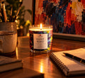 Velvet Roast candle glowing on artist desk with paint brushes