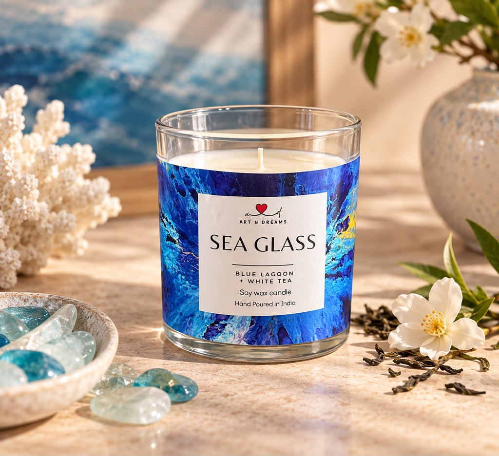 Sea Glass candle glowing warmly beside a painting on a wooden dresser